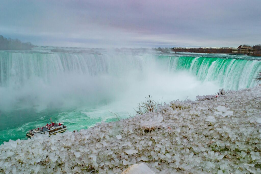 Frozen Niagara Falls with ice formations and boat below, capturing winter's beauty.
