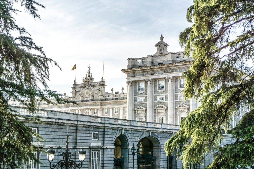 View of the Royal Palace of Madrid with surrounding trees under a clear sky.