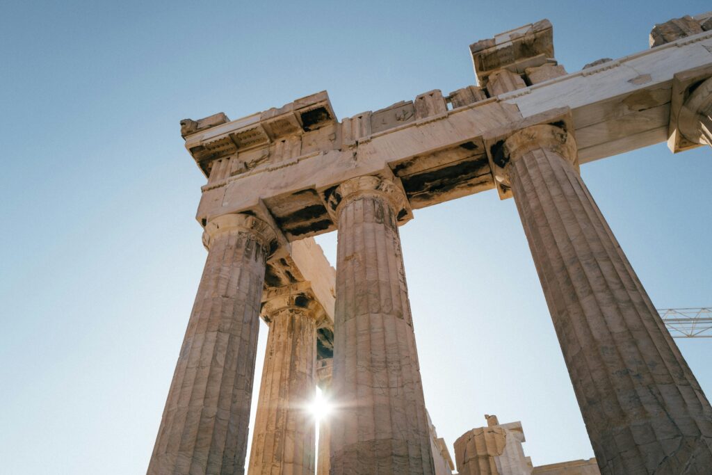 Low angle view of ancient Parthenon columns with sunlight peeking through, Athens, Greece.