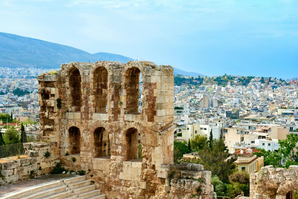 The iconic Odeon of Herodes Atticus in Athens with the city skyline and mountains in the background.