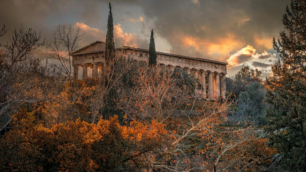 Dramatic sunset view of Hephaestus Temple surrounded by autumn foliage in Athens, Greece.