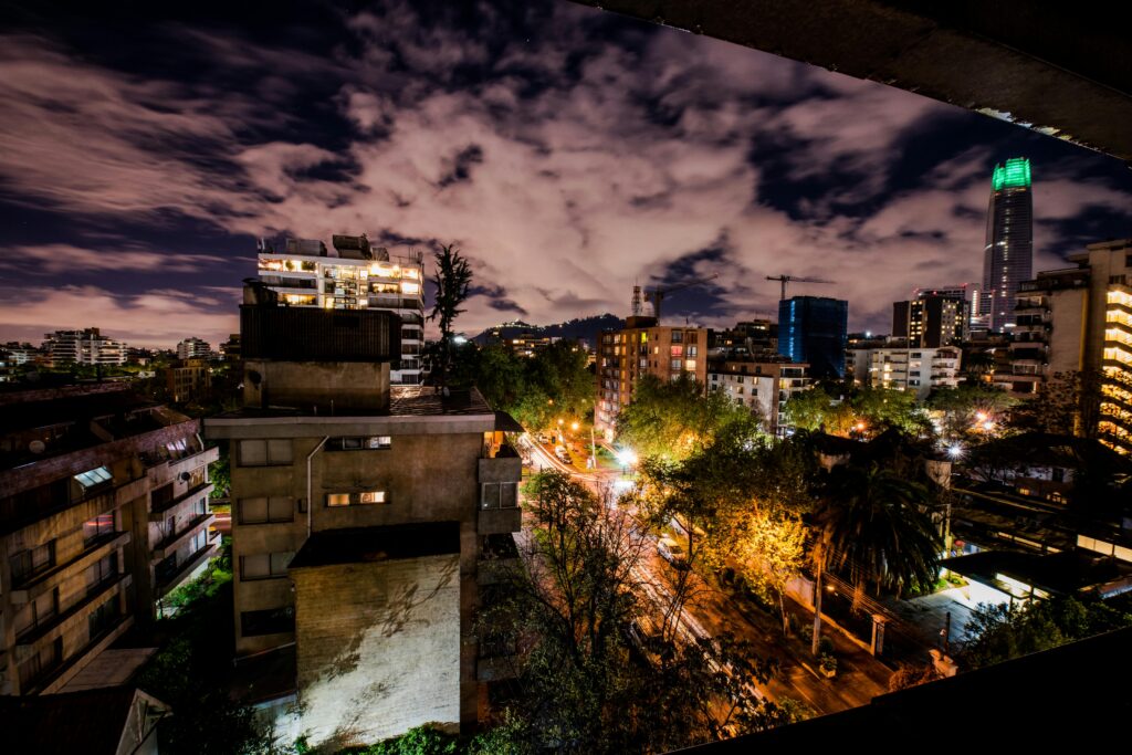 Dramatic night view of Santiago's skyline with lit buildings and cloudy sky.
