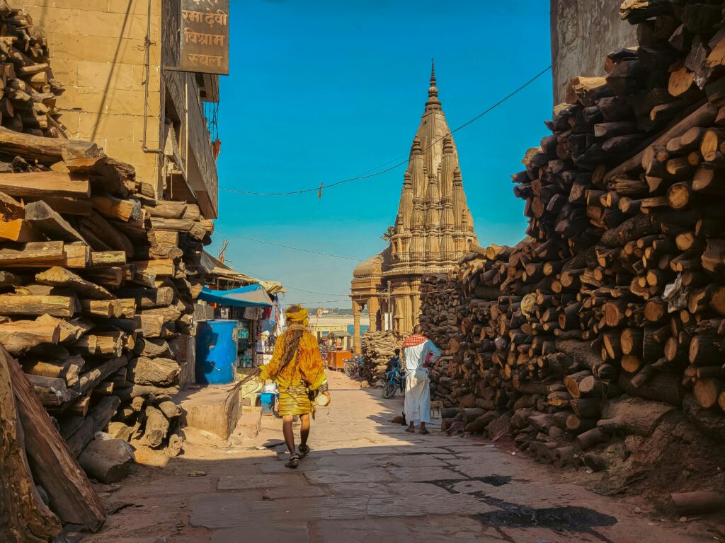 Street scene in Varanasi with wood piles and temple in view, showcasing daily life.