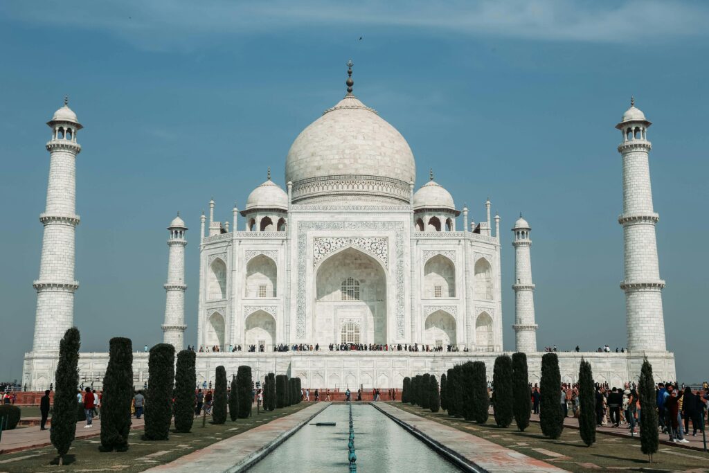 From below of famous facade of Taj Mahal cathedral and national mausoleum of India with decoration on stone walls near pond and trees under serene sky