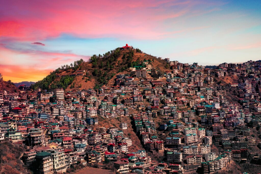 Majestic aerial view of Shimla, India with colorful buildings against a vibrant sunset sky.
