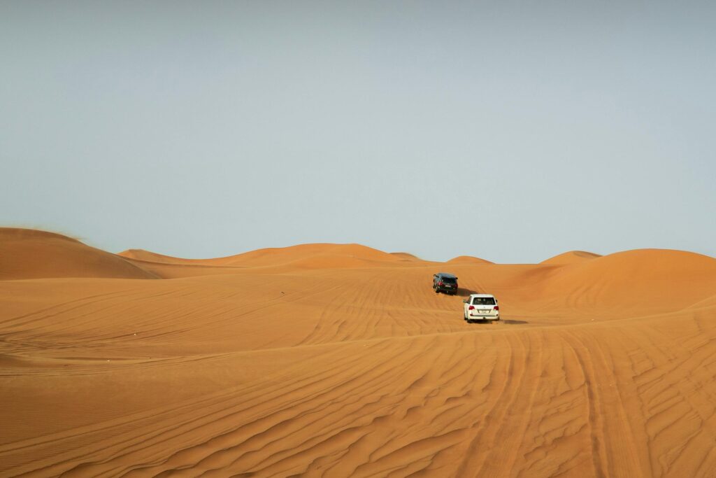 SUVs tread the stunning golden dunes of Dubai under a clear sky, capturing the essence of adventure.