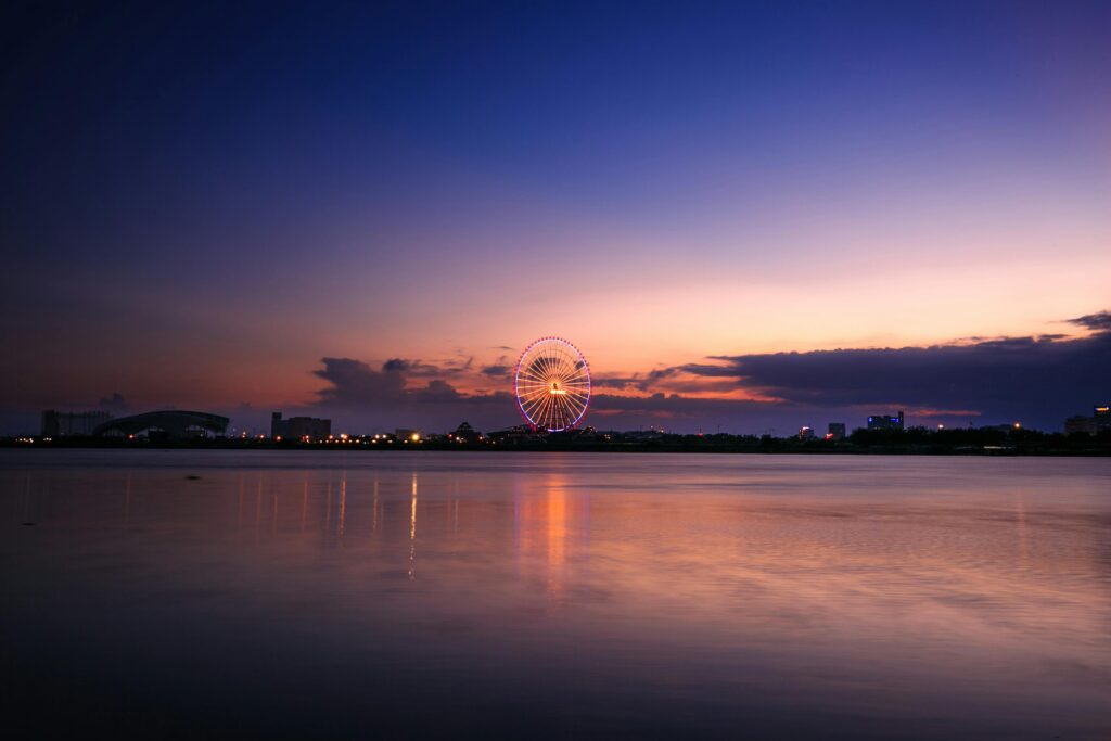 A captivating view of a ferris wheel reflecting over tranquil waters at sunset.