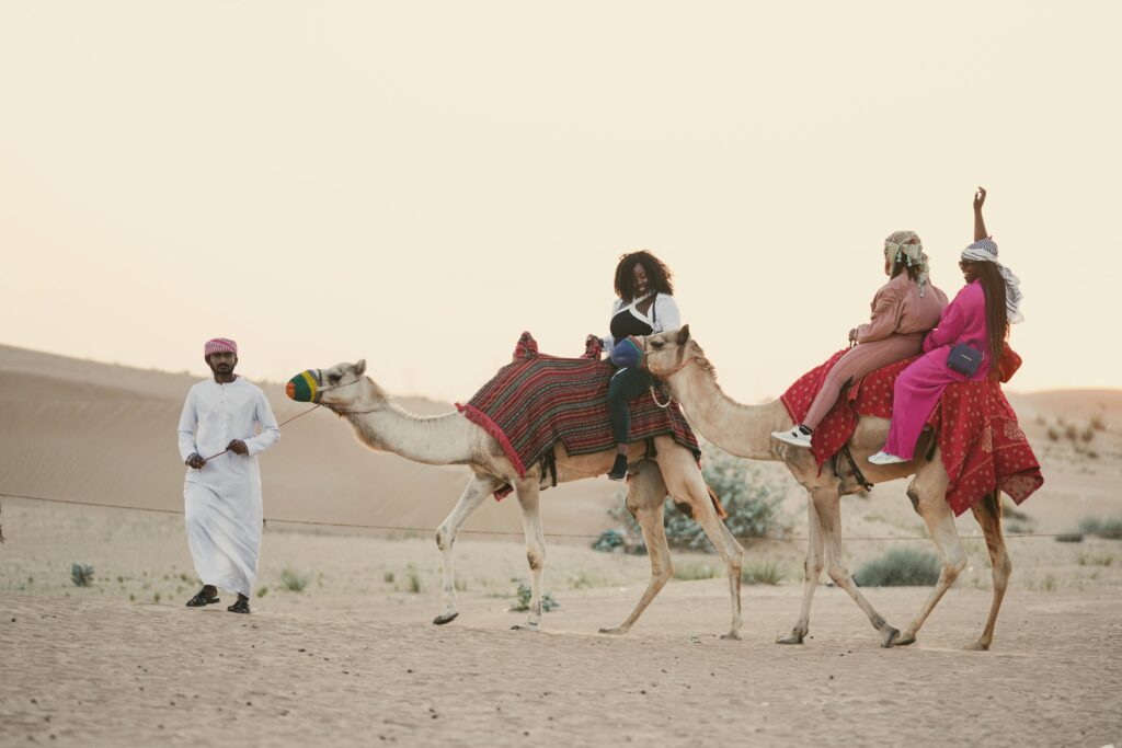 Women enjoying a camel ride adventure in the scenic Dubai desert at sunset.
