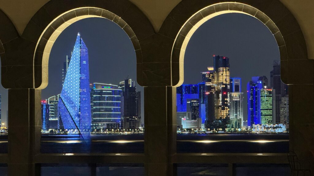 Stunning night view of Doha skyline seen through decorative archways, reflecting vibrant city lights.