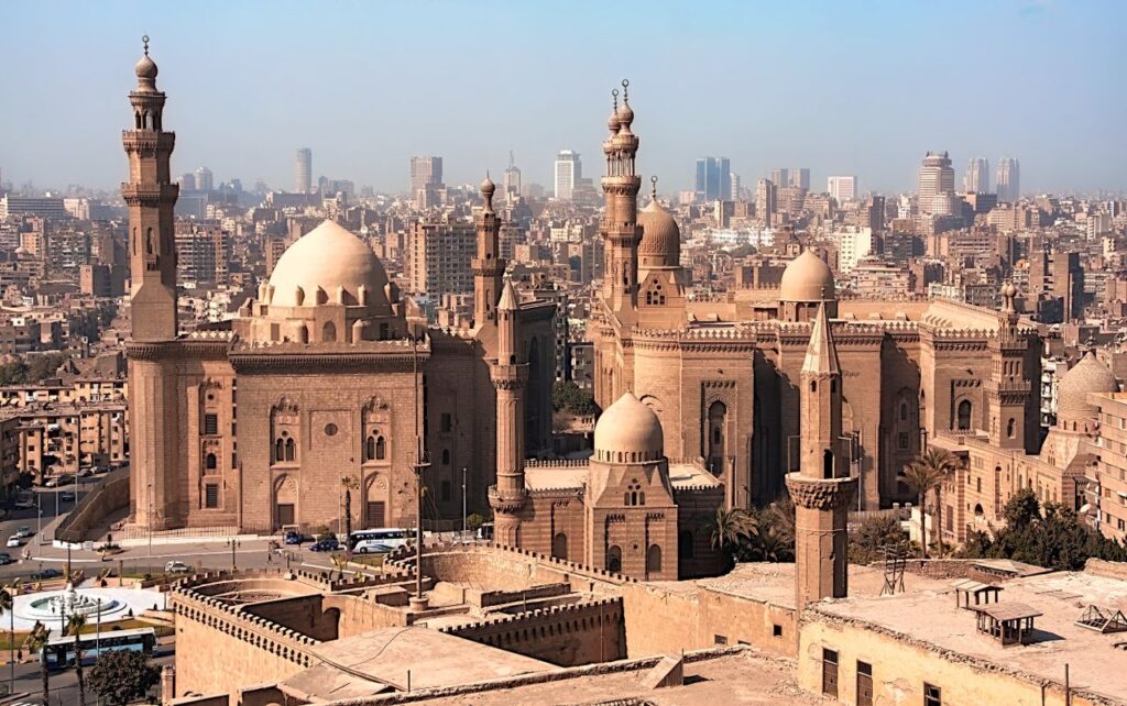 Aerial view of historic mosques with Cairo cityscape backdrop, showcasing Islamic architecture.