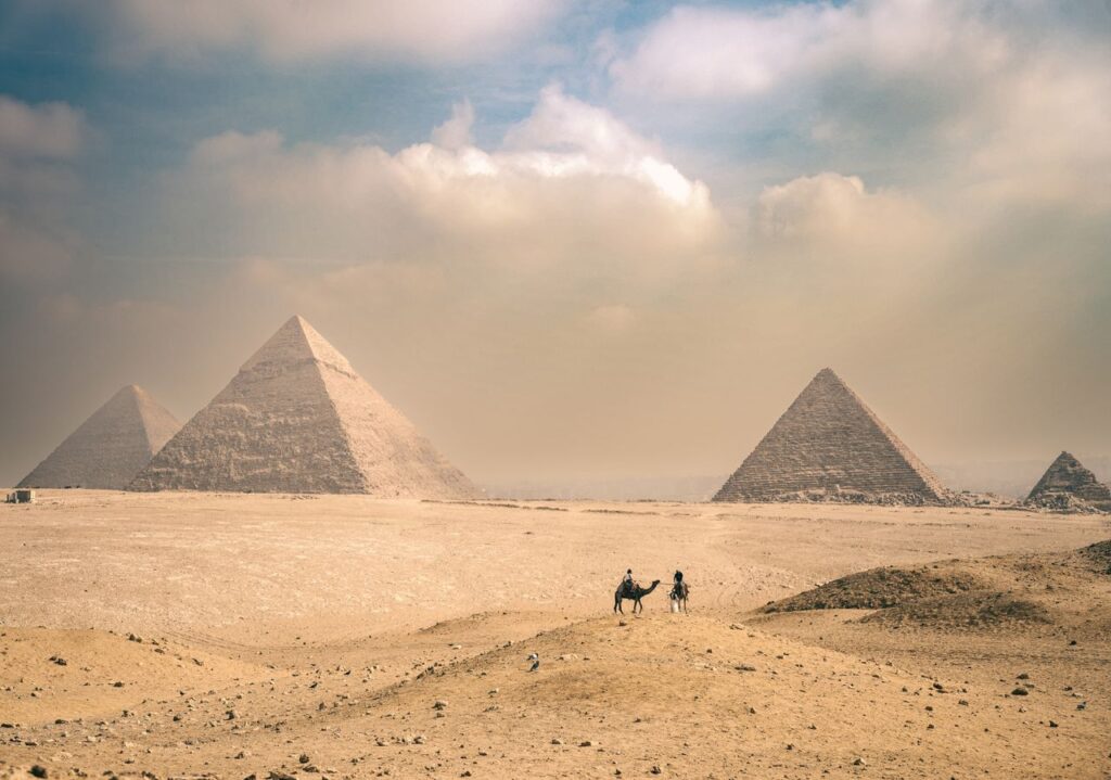 Explore the majestic Pyramids of Giza under a sunny sky with distant travelers on camels.