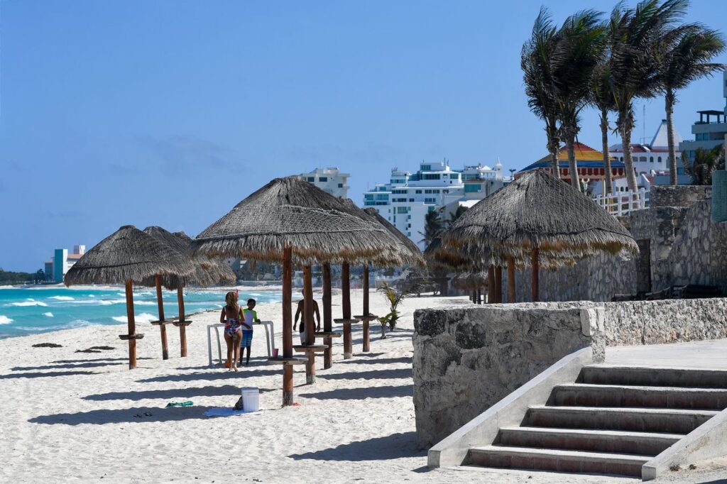A sunny beach scene in Cancún, Mexico featuring palapas, sandy shore, and vibrant ocean waves.