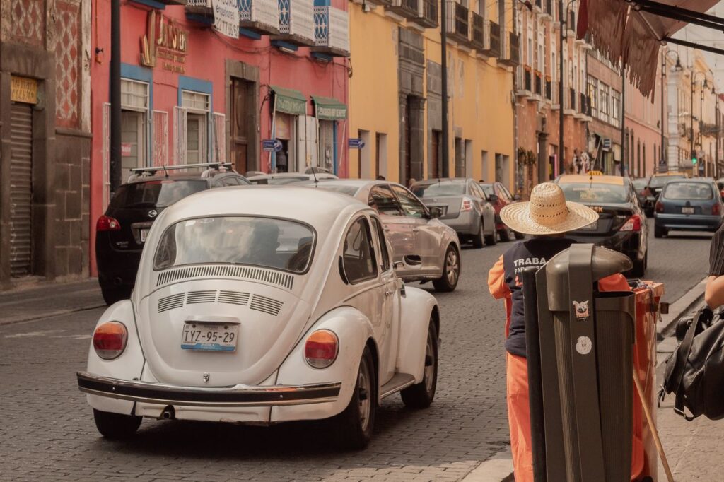 A classic white Volkswagen Beetle driving through the colorful streets of Puebla, Mexico.